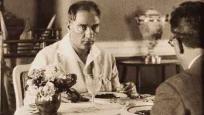 Atatürk at the table while travelling, in a white shirt; flowers and a glass of water on the table — 1930s archive photograph
